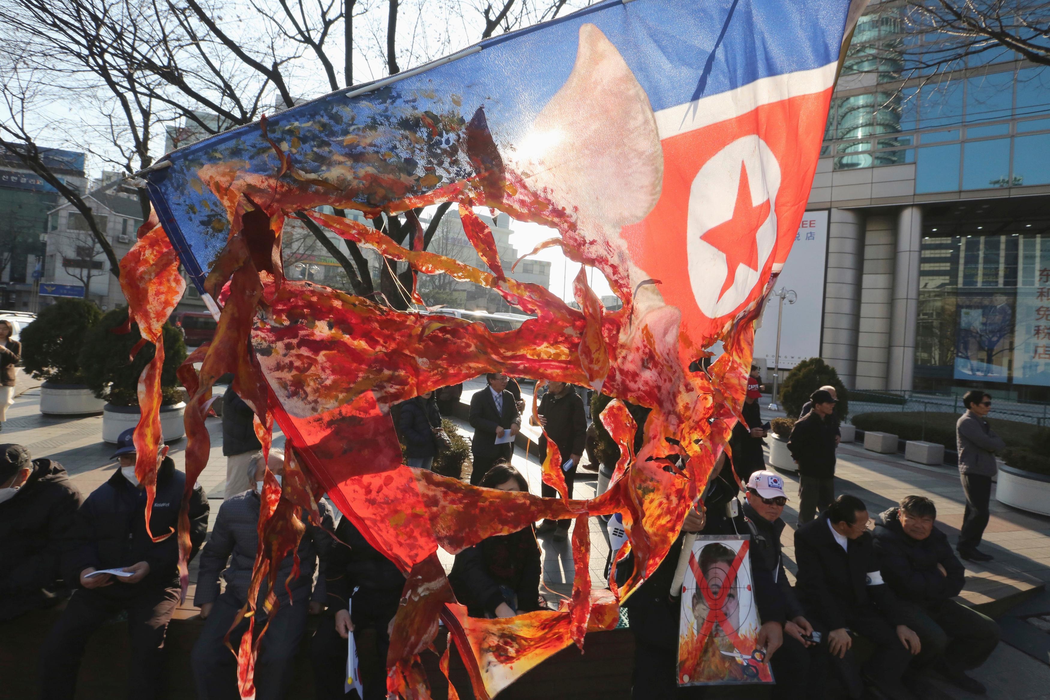 a south korean protester holds a defaced north korean flag